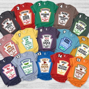 May include: A collection of fifteen short-sleeved t-shirts in various colors, each featuring a graphic print of a condiment bottle label with unique text such as Spicy Chipotle Sauce, Toasted Sesame Oil, Dark Chocolate Sauce, and Szechuan Sauce.