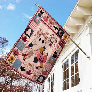 May include: A rectangular garden flag featuring a patchwork design with a central ghost character wearing a floral bow and holding a jack-o'-lantern bucket. The text Spooky Season is printed on the right. Icons include cats, bats, pumpkins, and candy corn.