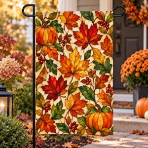 May include: A rectangular garden flag featuring a stained glass style pattern of orange pumpkins, red and yellow maple leaves, and clusters of small red berries. The design is set against a light cream background with dark outlines.