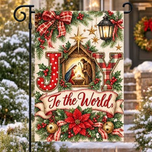 May include: A rectangular garden flag featuring the word JOY with a nativity scene inside the letter O. The text To the World is written on a banner below. The design includes red plaid bows, holly, poinsettias, and a lantern.