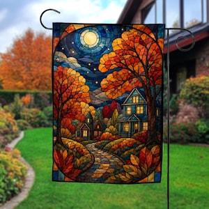 May include: A rectangular garden flag featuring a stained glass style illustration of a house at night during autumn. The scene includes a full moon, a stone path, and trees with orange and red foliage. The house windows are glowing with warm light.