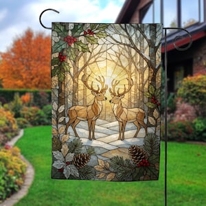 May include: A rectangular garden flag featuring a stained glass style illustration of two deer standing in a snowy forest. The scene includes holly leaves with red berries and pinecones at the corners, with a bright sun glowing in the background.