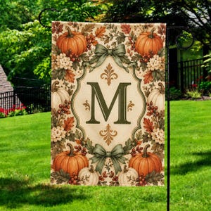 May include: A rectangular garden flag featuring a central cream-colored panel with a large dark green letter M. The border is decorated with orange pumpkins, white flowers, green leaves, and dark green bows at the top and bottom corners.