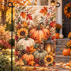 May include: A rectangular garden flag featuring a vibrant autumn scene with orange, white, and green pumpkins, yellow sunflowers, pinecones, red berries, and colorful fall leaves. A black metal lantern with a lit candle sits among the pumpkins.