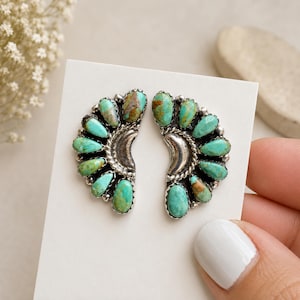 May include: A pair of silver earrings featuring a crescent moon shape surrounded by teardrop-shaped turquoise stones. Each earring has a central polished silver crescent with a twisted rope border and a fan of natural blue-green turquoise cabochons.