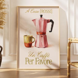 Puede incluir: Una lámina enmarcada que muestra una cafetera italiana rosa y una taza de café bicolor amarilla y roja. El texto A Casa [ROSSI] aparece en la parte superior, y el texto Un caffè Per Favore está impreso en letras doradas en la parte inferior.