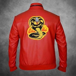 Può includere: Una giacca rosso acceso con colletto alto e polsini a coste. Il retro presenta una grande toppa ricamata di un cobra giallo e nero con la scritta Cobra Kai in lettere gialle, centrata sul materiale rosso dall'aspetto simile alla pelle.