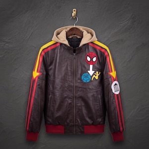May include: A dark brown leather jacket with a beige hood, featuring yellow and red racing stripes on the sleeves. The chest displays a Spider-Man mask patch, a blue spiderweb patch, a white arrow, and a yellow figure. A white circular patch with a black column icon is on the sleeve.