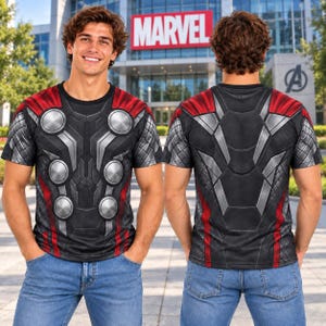 May include: A short-sleeved t-shirt featuring a graphic print of Thor's armour. The design includes a black base with red accents, silver metallic-look circular plates on the chest, and a textured pattern on the shoulders and sleeves.