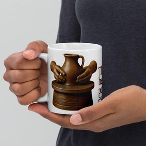 May include: A white ceramic mug featuring a graphic of brown hands shaping a brown clay pitcher on a wooden pottery wheel. The text on the side of the mug reads, "The best potter ever." The mug has a standard handle and a smooth, glossy finish.