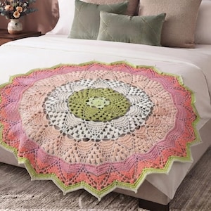 May include: A circular crochet blanket featuring a central sage green star pattern, surrounded by concentric rings of white, soft peach, and coral pink yarn. The outer edge is finished with a scalloped, pointed border in light lime green.