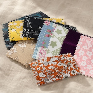 May include: A collection of rectangular fabric swatches with pinked edges, featuring various patterns including yellow floral, black and white line art, blue floral, green star print, solid deep purple, orange floral, and pink cherry blossom.