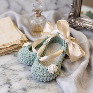 Peut inclure: Une paire de chaussons pour bébé en crochet vert sauge avec une semelle intérieure en tissu blanc à motif de cœurs. Chaque chausson est orné d'une petite fleur blanche en crochet et d'un long ruban de satin crème noué en nœud à la cheville.