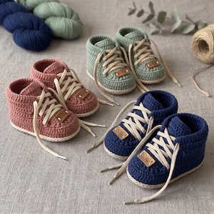 Peut inclure: Trois paires de baskets montantes crochetées à la main en rose poudré, vert sauge et bleu marine. Chaque paire présente des lacets couleur crème et une petite étiquette rectangulaire en similicuir marron sur la languette.