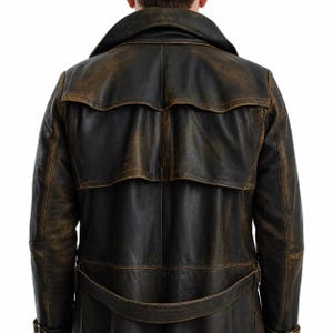 May include: A dark brown leather trench coat featuring a distressed finish, a wide collar, a back storm flap, and a matching belt at the waist. The coat displays visible stitching details and a weathered texture across the entire surface.