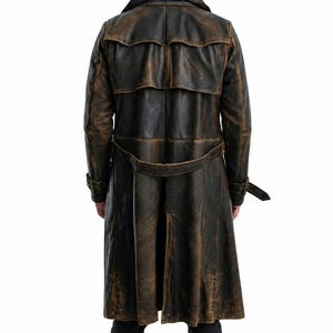 May include: A long, distressed dark brown leather trench coat featuring a wide collar, a back storm flap, and a matching waist belt with a buckle. The coat has long sleeves with buckled cuffs and a central back vent, showcasing a worn texture.