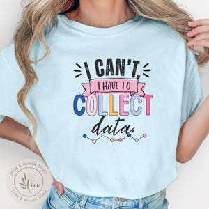 May include: A light blue t-shirt featuring the black text I CAN'T, I HAVE TO COLLECT data. The design includes a pink banner, multi-colored letters in blue, pink, and yellow, and a small line graph graphic with circular data points at the bottom.