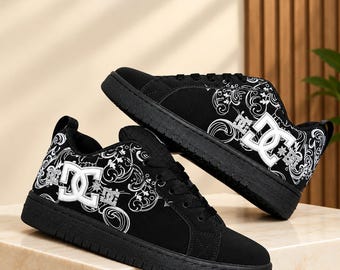 May include: A pair of black sneakers featuring a white DC logo on the side and a white swirling floral pattern across the upper. The shoes have black laces, a black sole, and a padded collar. The design includes a repeating white graphic print.
