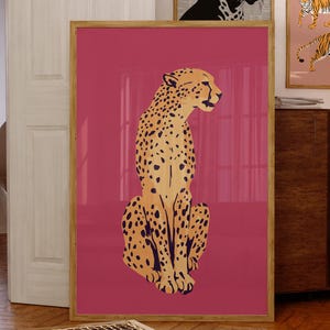 May include: A large framed vertical wall art print featuring a stylised illustration of a spotted cheetah in shades of tan and black, set against a solid deep pink background. The artwork is displayed in a light-coloured wooden frame.