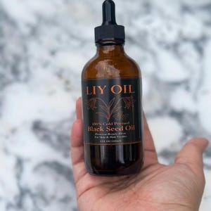 Puede incluir: Un frasco cuentagotas de vidrio ámbar que contiene aceite de semilla negra LIY OIL 100% prensado en frío. La etiqueta negra presenta texto de color cobre y una ilustración botánica. El frasco indica 4 FL OZ (118ml) para piel y cabello.