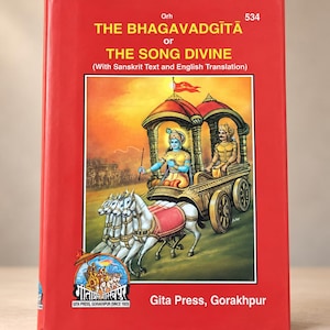 Puede incluir: Un libro de tapa dura rojo titulado The Bhagavadgītā or The Song Divine with Sanskrit Text and English Translation. La portada presenta una ilustración de un carro tirado por cuatro caballos blancos, con dos figuras dentro, y el logo de Gita Press.