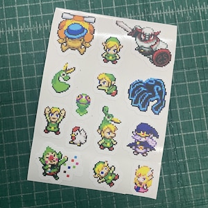 Pode incluir: Uma folha de autocolantes branca com quinze designs individuais de pixel art. Os gráficos incluem várias personagens com túnicas verdes, uma galinha branca, uma criatura azul, um feiticeiro escuro, uma figura blindada vermelha e branca.