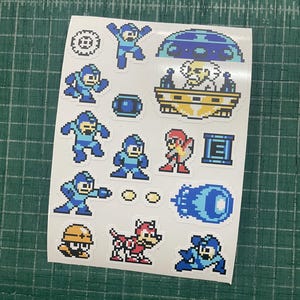 Könnte beinhalten: Ein Aufkleberbogen mit verschiedenen Pixel-Art-Figuren und Gegenständen aus der Mega Man-Videospielserie, darunter Mega Man in verschiedenen Posen, Dr. Wily in seiner Kapsel, der Roboterhund Rush sowie diverse Power-Up-Symbole in Blau und Rot.