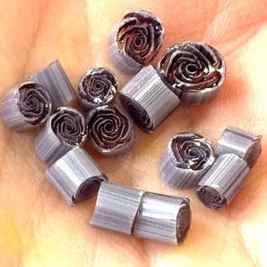 Op de afbeelding: Een verzameling kleine, zilverkleurige, gerolde metalen rozen. De rozen liggen in een stapel op een hand.