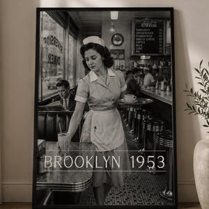 Könnte beinhalten: Ein schwarz-weiß gerahmter Wandkunstdruck, der eine Diner-Szene aus den 1950er Jahren zeigt, mit einer Bedienung in Uniform, die ein Tablett und ein Glas hält. Der Text BROOKLYN 1953 ist unten eingeblendet. Im Hintergrund sind ein Tresen und Barhocker zu sehen.