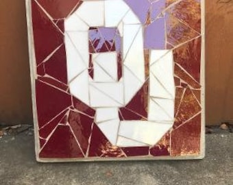 May include: A mosaic tile artwork featuring the letter "O" in white against a red background. The "O" is made up of smaller white tiles, and the background is made up of smaller red tiles.