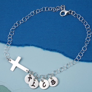 May include: Silver chain bracelet with a cross charm and five small charms with the letters T, I, C, O, and B.