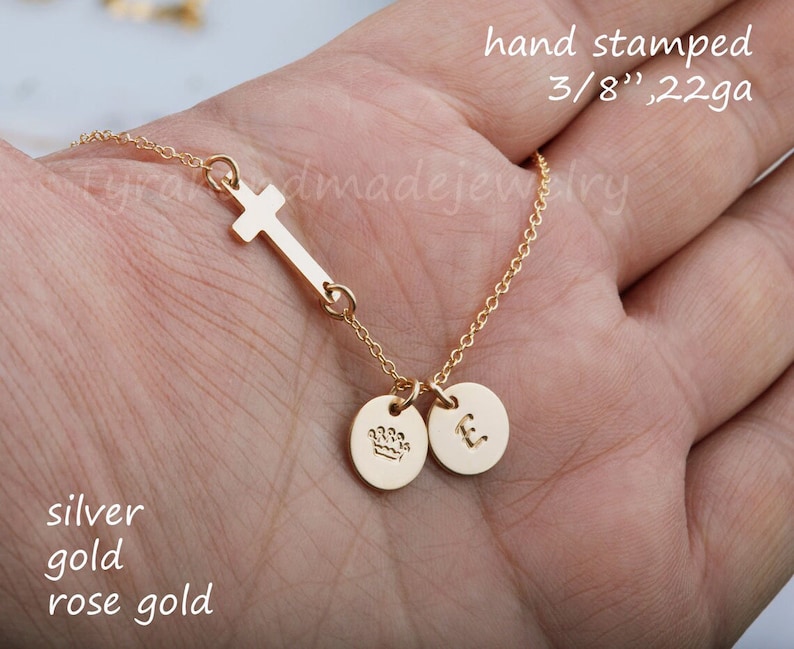 May include: A gold necklace with a small cross charm and two round charms, one with a crown and the other with the letter "E". The necklace is hand-stamped and measures 3/8" in length. The necklace is available in silver, gold, and rose gold.