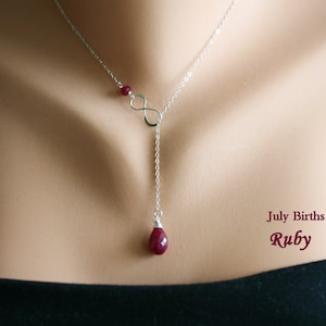 May include: A silver infinity necklace with a dangling ruby gemstone. The necklace is on a model's neck and the text "July Birthstone Ruby" is visible below the necklace.