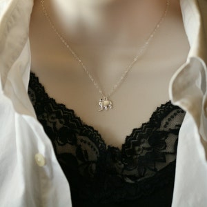 May include: A silver-toned necklace featuring a small, flat elephant pendant suspended from a delicate, thin chain. The pendant is shaped like a stylized elephant in profile, showcasing a smooth, reflective metallic surface and simple, clean lines.