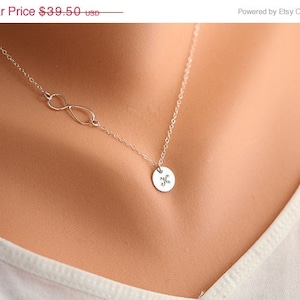 Könnte beinhalten: Eine silberne Halskette mit einem Unendlichkeits-Anhänger und einem kleinen runden Anhänger, auf dem der Buchstabe "K" eingraviert ist.