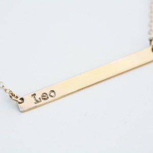 May include: A gold bar necklace with the name "Leo" engraved on it.