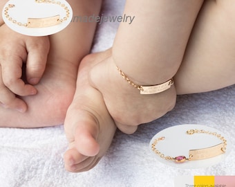 May include: Gold baby bracelet with a personalized nameplate and a small pink gemstone. Three colors are available.