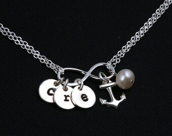 May include: Silver necklace with an infinity symbol charm, three small round charms with the letters "cre" engraved on them, a small anchor charm, and a single pearl.