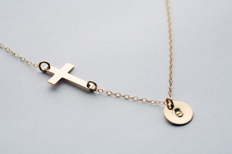 May include: A gold chain necklace with a simple cross pendant and a small round disc pendant.