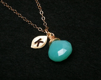 Puede incluir: Un collar de cadena dorada con un colgante de piedra turquesa y un dije de hoja de oro con la letra "K" grabada.