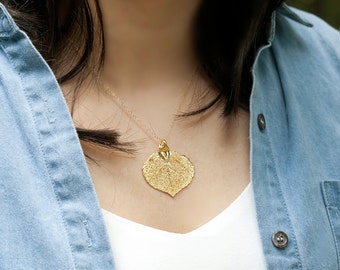 Puede incluir: Un collar de oro con un colgante en forma de hoja. El colgante es texturizado y tiene un diseño delicado.