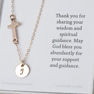May include: Gold necklace with a small cross charm and a round charm with the letter 'J' engraved on it. The necklace is in a white box with a thank you message.