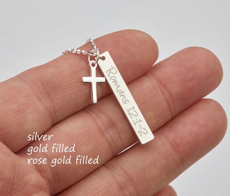 May include: Silver necklace with a small cross charm and a bar pendant engraved with "Romans 12:1-2".