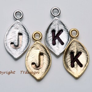 May include: Four leaf-shaped charms with different letter engravings. Two charms are silver with a gold letter 'J' and a purple letter 'K'. Two charms are gold with a gold letter 'J' and a purple letter 'K'.