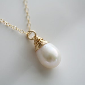 May include: A delicate gold chain necklace with a single white pearl pendant. The pearl is wrapped in gold wire.