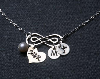 Puede incluir: Collar de plata infinito con un dije en forma de corazón grabado con "M&R" y dos dijes redondos con las letras "M" y "J". Una sola perla cuelga del símbolo del infinito.