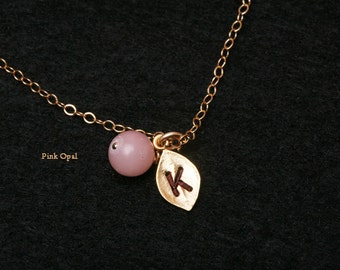 Puede incluir: Un collar de cadena de oro con una cuenta de ópalo rosa y un dije de hoja de oro con la letra "K" grabada.
