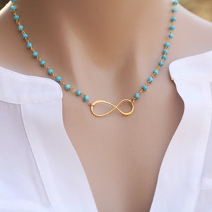 Könnte beinhalten: Eine Halskette mit einem goldenen Unendlichkeits-Anhänger und türkisfarbenen Perlen.