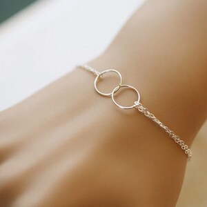 May include: A delicate silver chain bracelet featuring two interlocking circles. The circles are simple and elegant, making this a minimalist piece of jewellery.