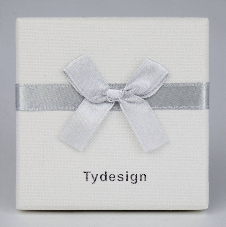 May include: A white gift box with a silver ribbon and bow. The box has the word "Tydesign" printed on the front.